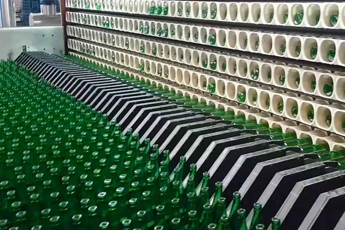 Esteira automatizada com garrafas verdes alinhadas, ilustrando eficiência e automação em linhas de envase.