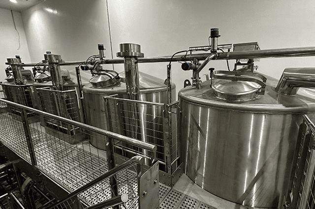 Tanques de aço inoxidável interligados, exemplificando sistemas completos para produção em cervejarias e fábricas de refrigerantes.